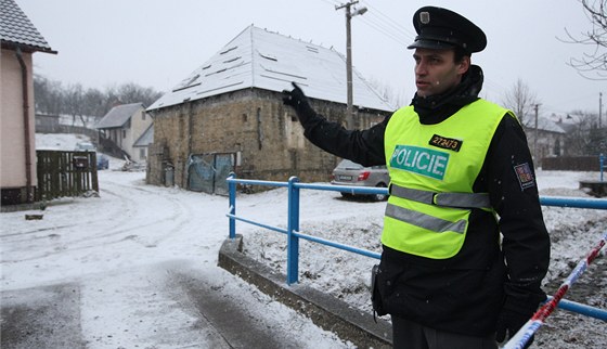 Policista hlídkuje u usedlosti s tajným skladem zbraní (vlevo vzadu).