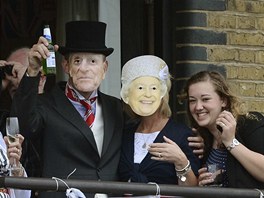 Lidé s maskami britské královny mávají na prvod z ochozu Tower Bridge