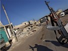 Syrský rebel na motocyklu zdraví zdvieným AK-47, zatímco projídí troskami