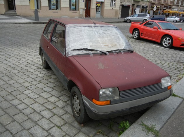 Auto s rozbitým sklem stojí v ulici Dejvická blízko křižovatky Jaselská na