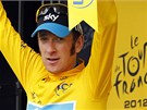 Cyklista Bradley Wiggins ve lutém dresu na pódiu mává fanoukm.