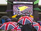 Diváci schovaní pod detníky sledují na obrazovce tenisové utkání v zasteeném
