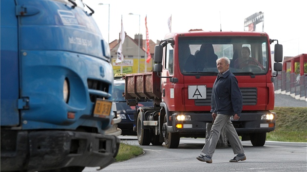 Na silnici bez vyznačeného přechodu pro chodce se lidé potkávají s nákladními auty. 