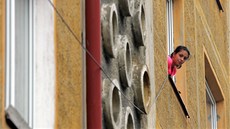 Z okna svého bytu kouká jedna z nájemnic zdevastovaného paneláku, který za 4