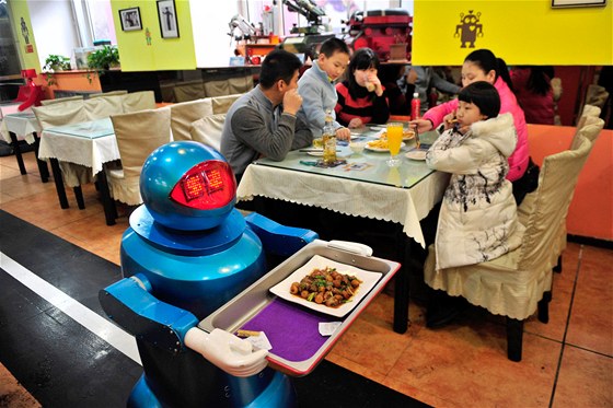 Roboti s tácy krouží po pásech mezi stoly.