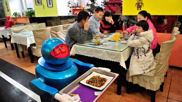 Roboti s tácy krouží po pásech mezi stoly.