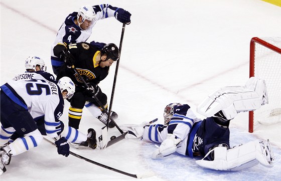 Ondej Pavelec z Winnipegu vytlauje puk, který se za jeho záda snaí dostat