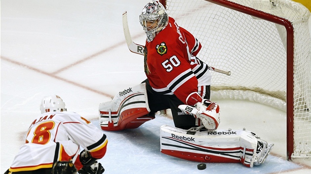 LEVM BETONEM. Glman Chicaga Corey Crawford spn zasahuje proti stele Matta Stajana z Calgary.