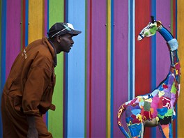 Řezbář Jackson Mbatha s ještě nedokončenou velkou hračkou žirafy před malovanou...