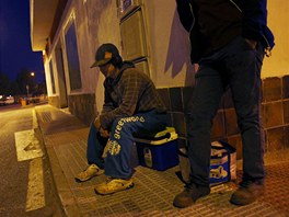 Day labourer Jorge Ibanez, 20, (L) waits to be picked up for a day's work...
