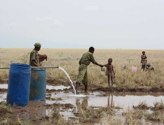 Keňský policista podává vodu žíznivému dítěti u vrtu v Lotikipi. (Keňa, září