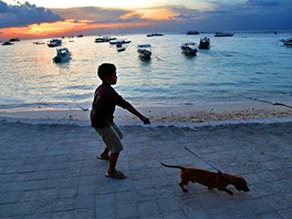 VENENÍ PI SOUMRAKU. Baliský chlapec vení svého psa tsn ped západem slunce.