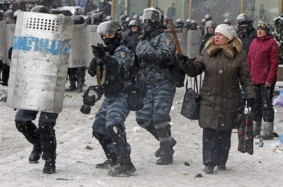 Žena v centru Kyjeva drží dřevený kříž, zatímco policisté míří zbraněmi na...