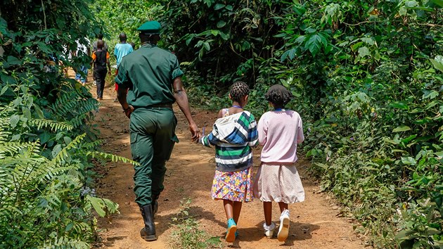 Děti v doprovodu strážců rezervace na cestě od autobusu za živými gorilami v záchranné stanici.