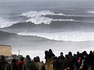 Lidé pozorují vlny, které se títí o pobeí u portugalského Nazaré...