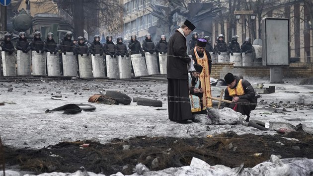 Pravoslavní kněží zapalují svíčky před kordonem policistů v centru hlavního města (13. února 2014).