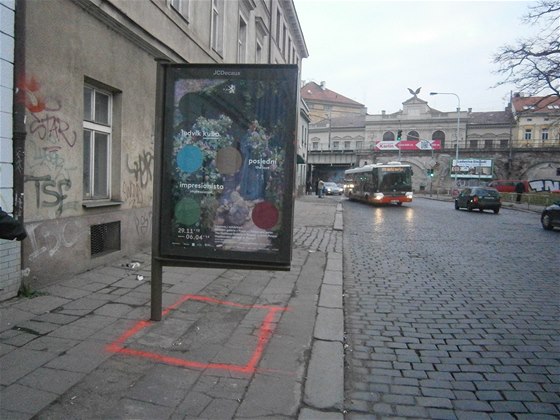 V ulici Prvního pluku pekáí na chodníku reklama.