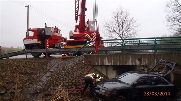 Automobil se dvma pasary skonil na boku v potoce pod mostkem (23. bezna 2014).