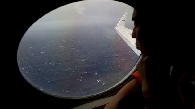 Člen japonské pobřežní stráže z okna letadla vyhlíží možné trosky letu MH370 na hladině (1. dubna 2014).