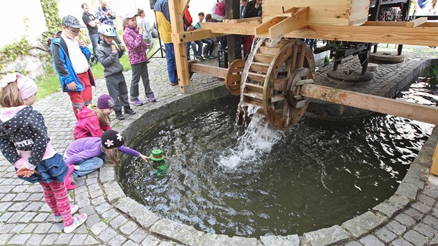 U mlýnského kola se z vody vynořuje vodník.