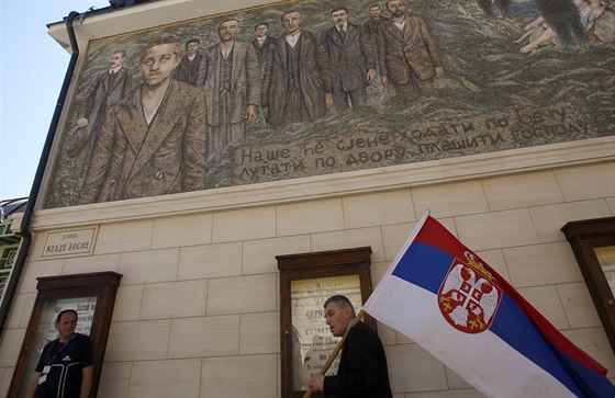Muž se srbskou vlajkou prochází pod mozaikou s portrétem Gavrilo Principa,...