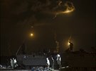 Izraeltí vojáci stojí okolo tank, zatímco je vidt kou a svtlo ze stelby v...