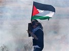 Mladá dívka kráí s palestinskou vlajkou po ulici zahalené slzným plynem ve...