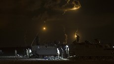 Izraeltí vojáci stojí okolo tank, zatímco je vidt kou a svtlo ze stelby v...