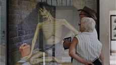 Turisté si prohlíí malbu znázorující mueného zajatce Rudých Khmér. Muzeum