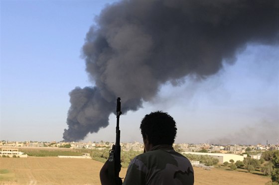 Jeden z bojovník libyjských milic pózuje se zbraní, zatímco za jeho zády...