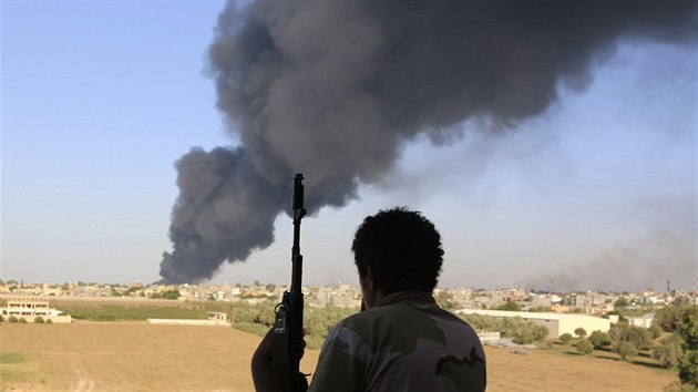 Jeden z bojovnk libyjskch milic pzuje se zbran, zatmco za jeho zdy stoup hust dm nad Tripolisem (2. srpna 2014).