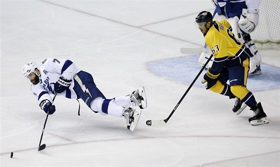 Radko Gudas z Tampy Bay padá a zárove odehrává puk, sleduje ho Mike Ribeiro.