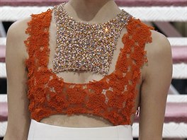 Detail bílých vlněných šatů, jejichž vrchní část tvoří oranžová krajka guipure...