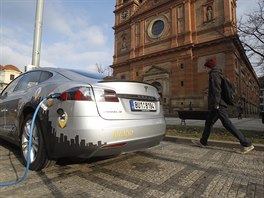 Elektromobil stoj� p�i dob�jen�  na chodn�ku. Na silnici z druh� strany je...