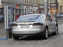 Elektromobil stoj� p�i dob�jen�  na chodn�ku. Na silnici z druh� strany je...