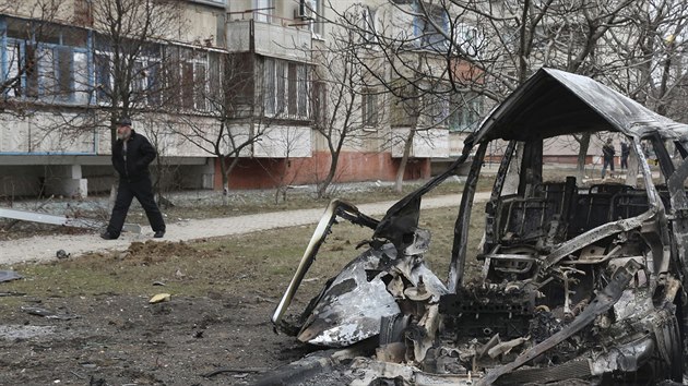 Muž prochází kolem ohořelého vraku auta po raketového útoku v Mariupolu (24. ledna 2015).
