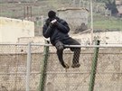 Africký uprchlík na plotu mezi Melillou a Marokem pojídá sendvi, který mu...