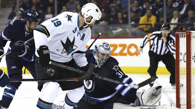 PARDN ZKROK. Brank Winnipegu Ondej Pavelec lap puk, ped nm Joe Thornton ze San Jose.