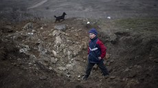 Chlapec z východoukrajinského Čermalyku prolézá kráter, který zůstal po bojích...
