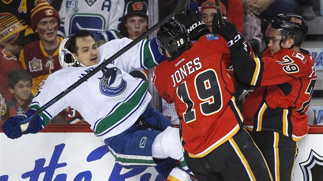 Luca Sbisa (vlevo) z Vanouveru pad po nrazu do dua Michael Ferland a David Jones z Calgary.