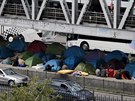An elevated metro passes over a bridge where migrants have established a...