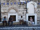 Lidé v Aténách sedící ped ortodoxním kostelem ozdobeným eckými vlajkami.