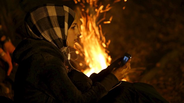 Migrantka poslouch� hudbu z mobiln�ho telefonu, zat�mco �ek� na mo�nost p�ej�t slovinsko-rakousk� hranice (28. ��jna 2015)