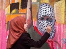 PROPAGANDA. Palestinka v pásmu Gazy maluje na ze zakuklence ozbrojeného noem....