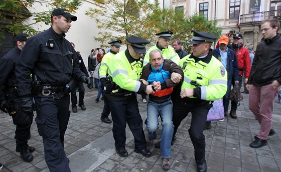 Policisté a stráníci vyvádjí Pavla Hradila ze shromádní komunist v Brn. Zlomil jim tam transparent.