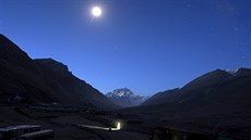 The first light of dawn illuminates Mount Everest as the moon shines above and...