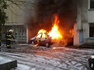 Hoící automobil v sousedství domu, kterému plameny pokodily fasádu.