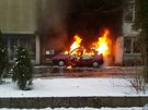 Hoící automobil v sousedství domu, kterému plameny pokodily fasádu.