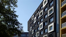Fasáda budovy je minimalisticky černá, s bílými okenními rámy.