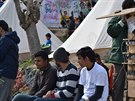 Migranti posedávají u místa pro nabíjení telefonu v centru tábora u hotspotu...